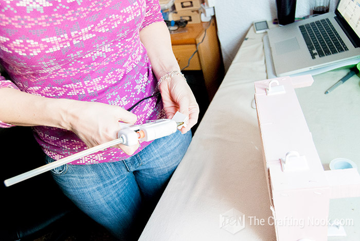 general view of person applying hot glue to a plastic hanger and the bottom wall of the fruit crate
