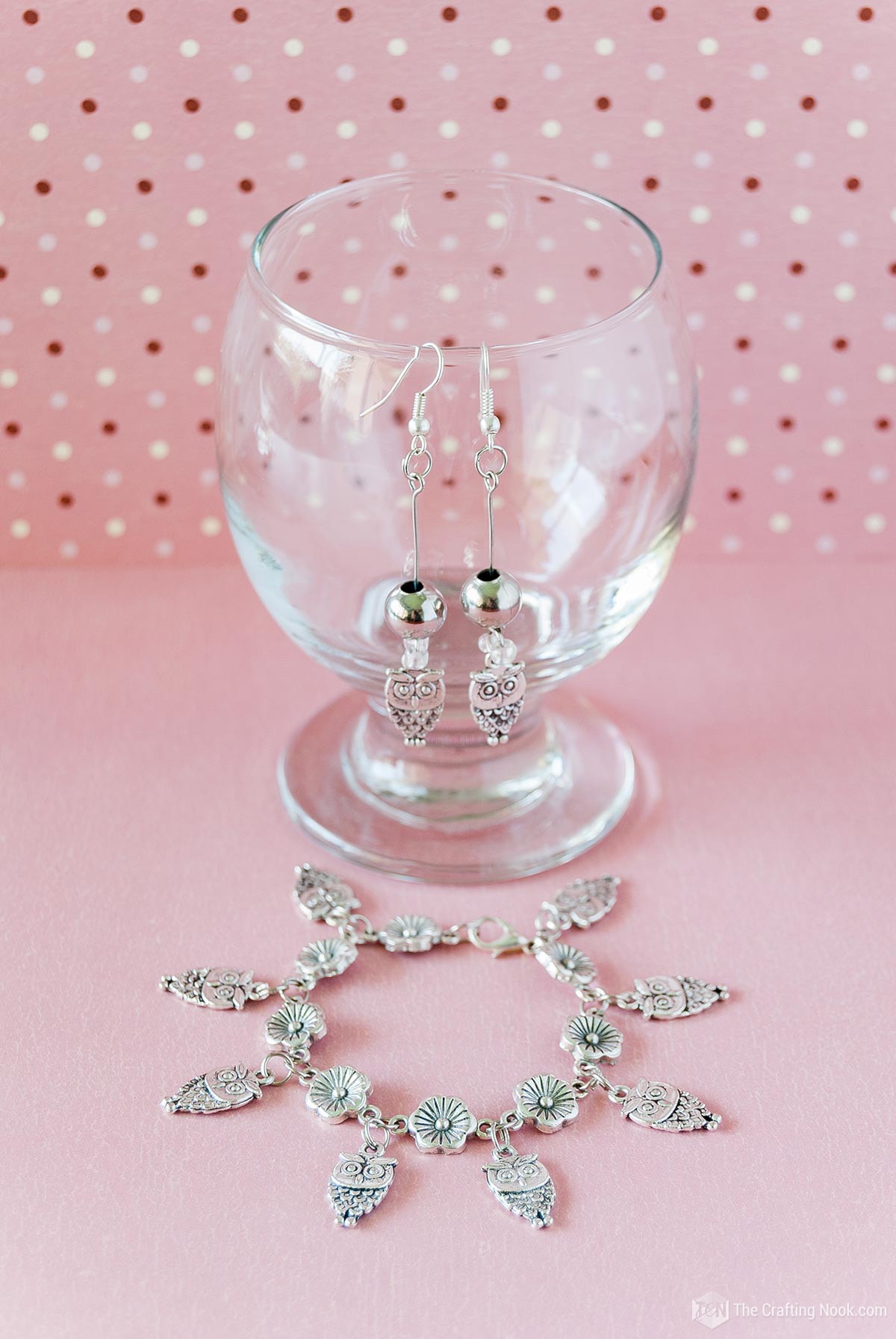 DIY Charm Bracelet on a pink background and Earrings hanging from a clear glass