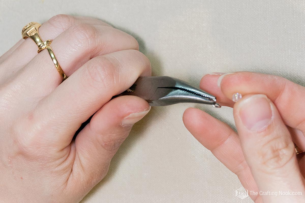 hand holding jump ring with pliers and in the other hand a bead