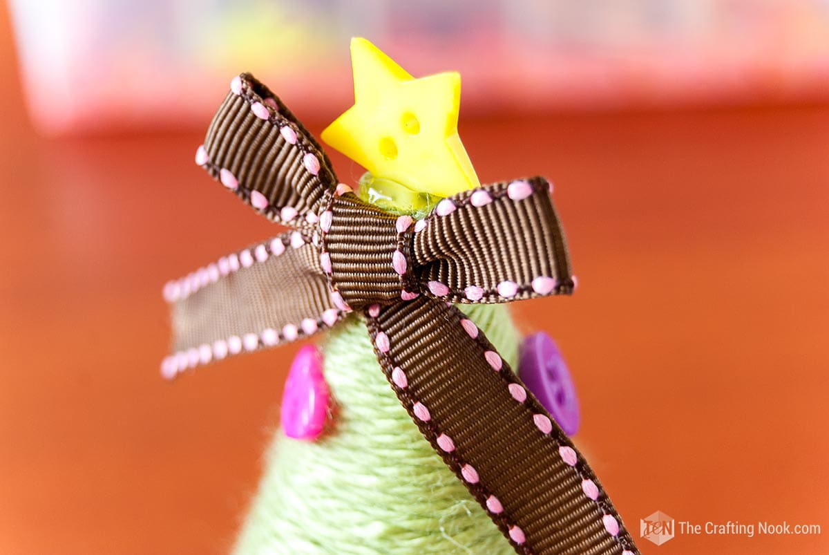 close view of the top of the tree with a bow and a yellow star-shaped button
