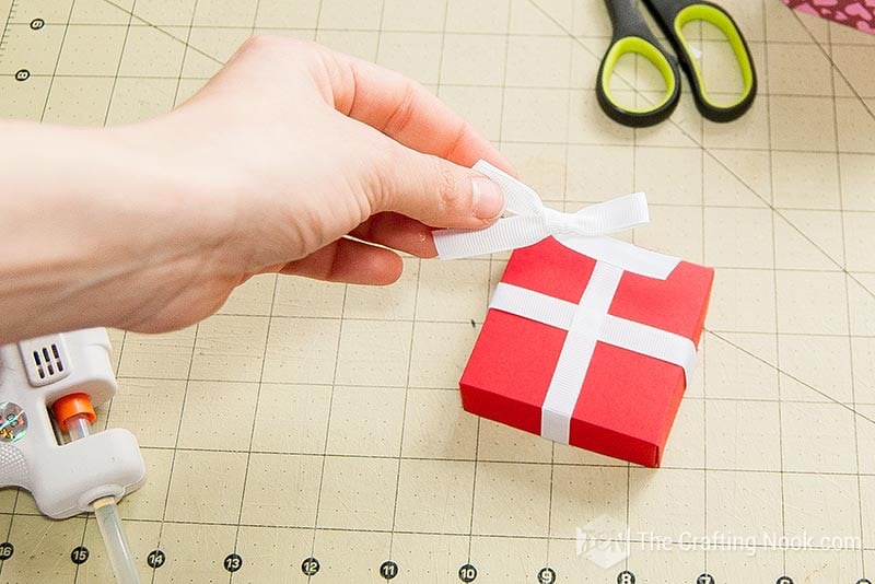 placing the ribbon bow on the lid on top of the crossing ribbons