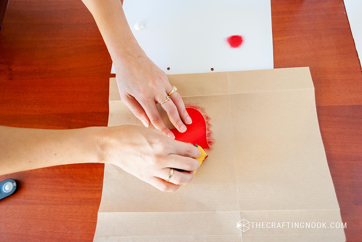 showing how to sponge paint onto the paper bag using a heart stencil
