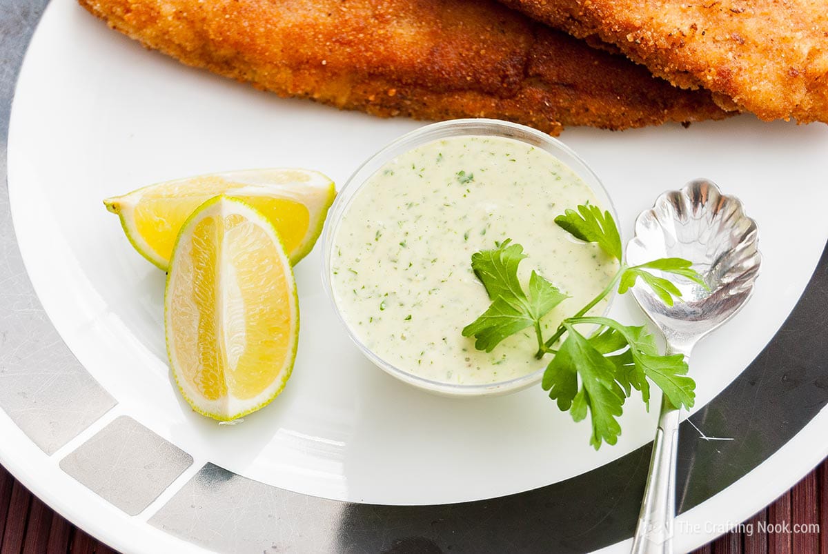 Overhead view of the Homemade Tartar Sauce in a cute cup next to lemons slices and breaded fried fish