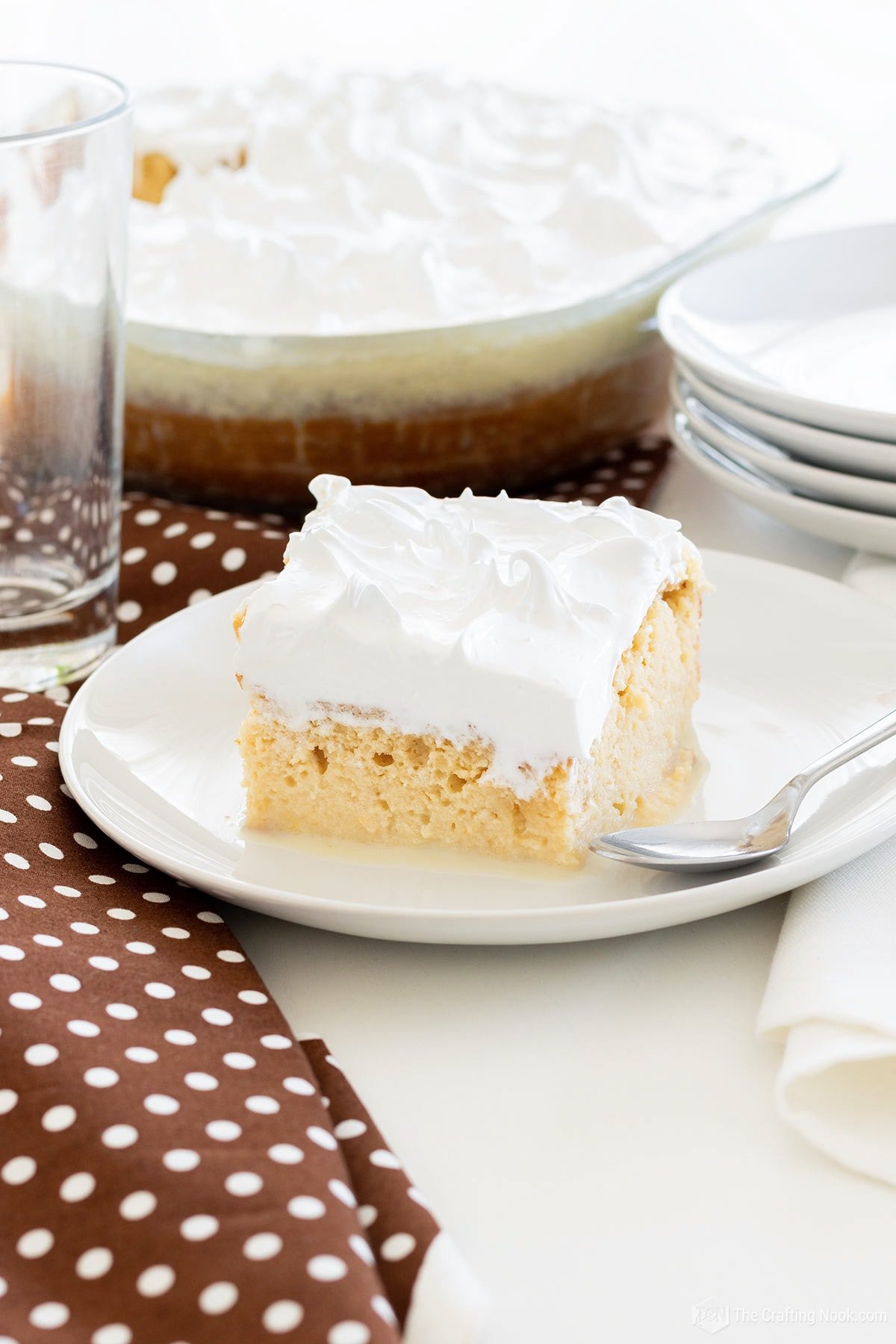 A squar piece of Tres Leches Cake (Three Milks Cake) in a white dish with the whole cake behind