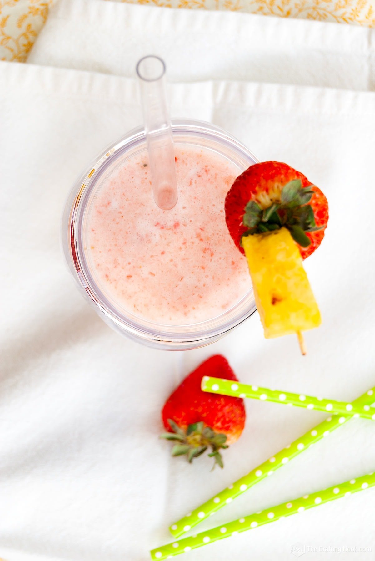 Overhead view of the Strawberry Pina Colada garnished with A strawberry and a pineapple wedge and a few straws laying around