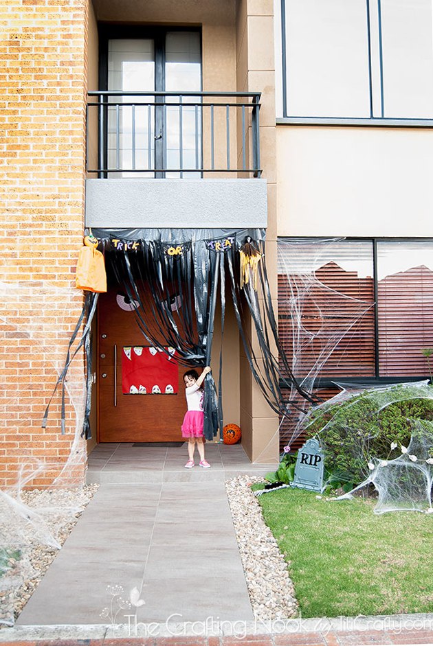 My girl grabbing the plastic curtain to let the Front Door Halloween Decor be visible