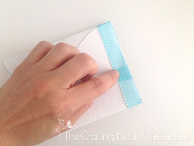 top view of a finger on the junction of the light blue ribbon wrapping the card
