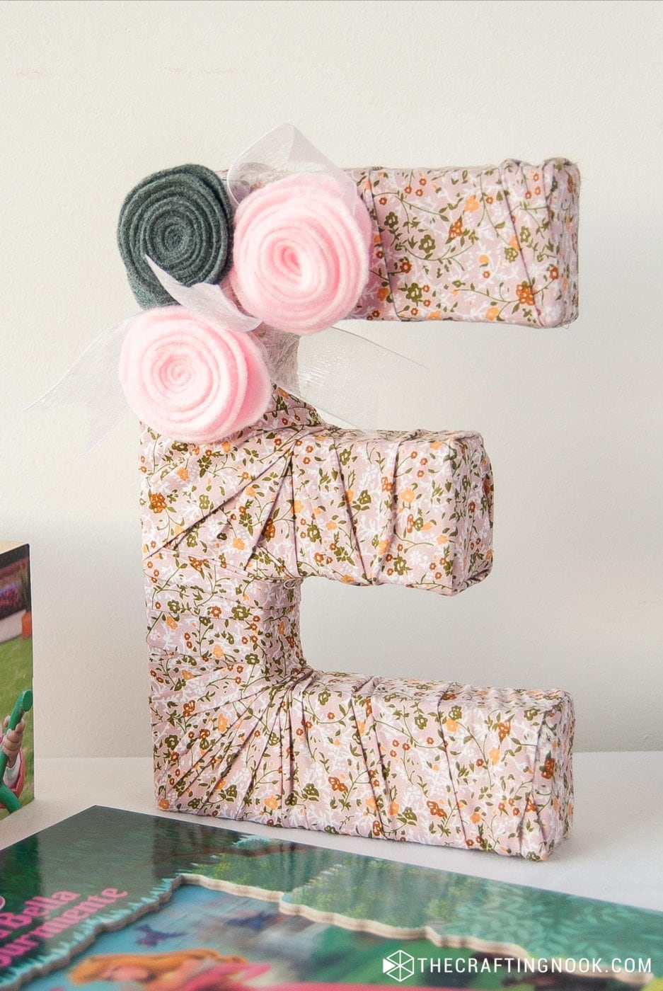 Closeup of DIY Fabric Covered Letters with flowers on a nightstand table between children book and a photoframe