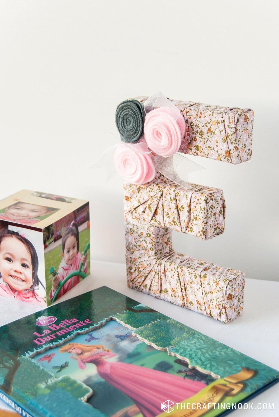 DIY Fabric Covered Letters with flowers on a nightstand table between children book and a photoframe