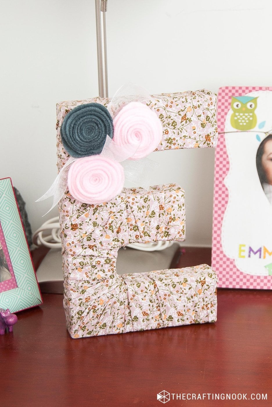 closeup of DIY Fabric Covered Letters with flowers on a nightstand table between photoframes