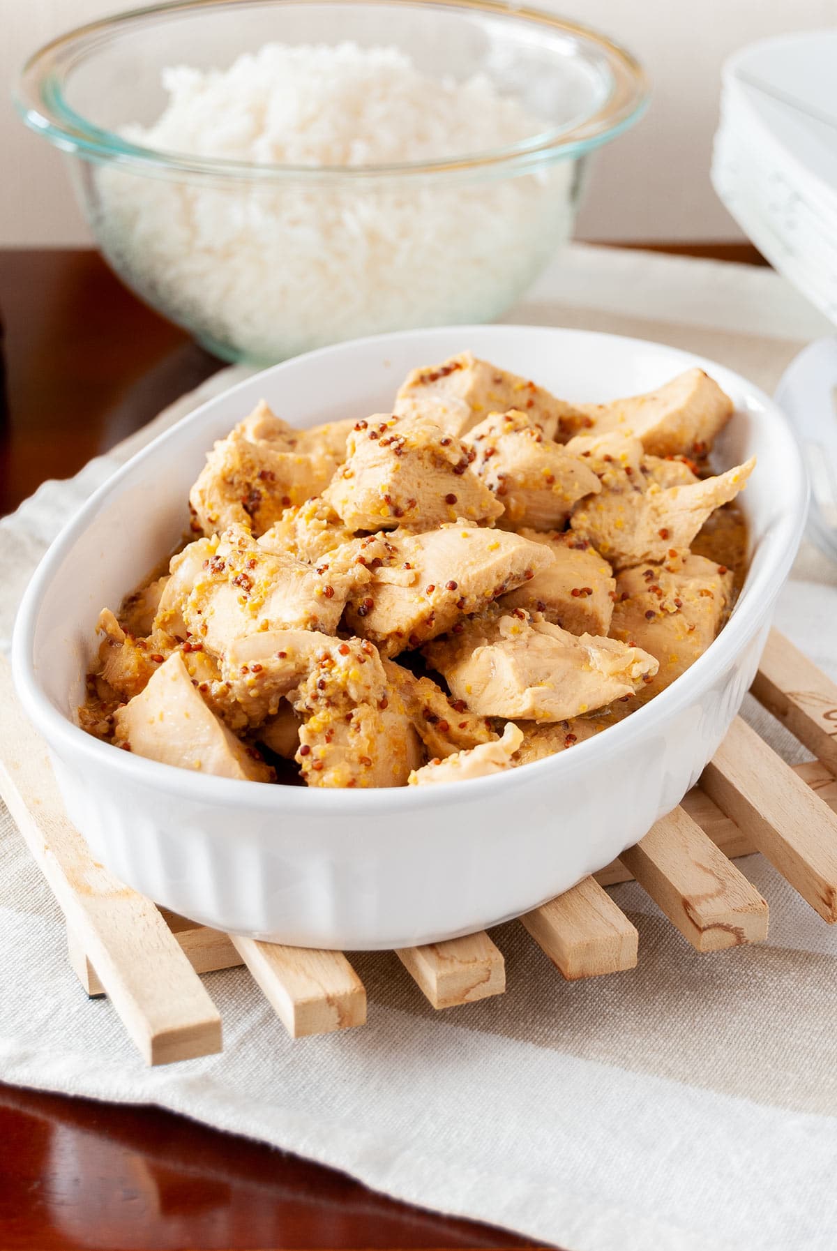 Closeup 45 degree shot of the Honey Mustard Chicken Marinade in a white ceramic dish with a bowl of rice in the back