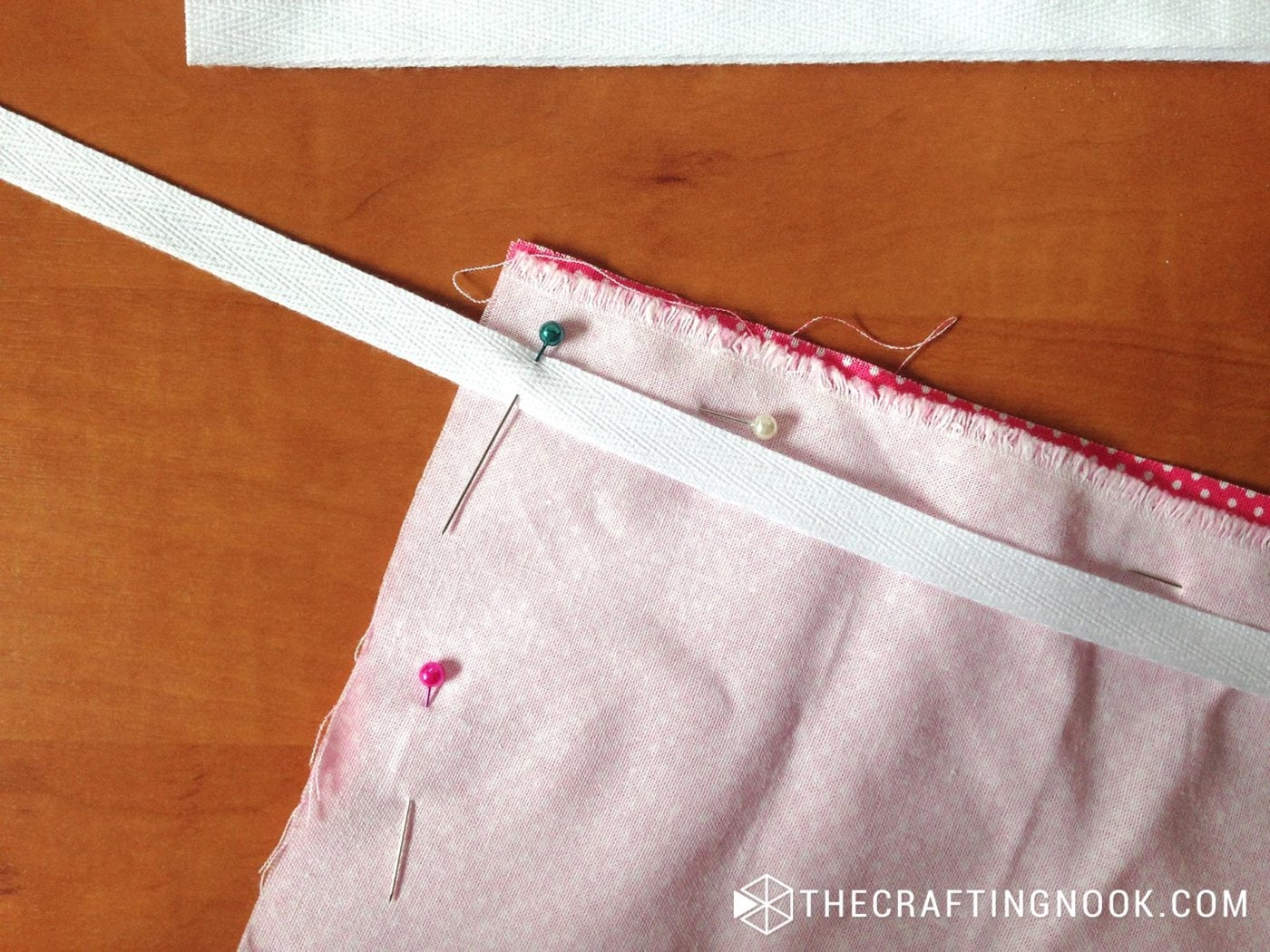 close up image of a corner of one of the quilt layers with a white ribbon and pins to hold them together
