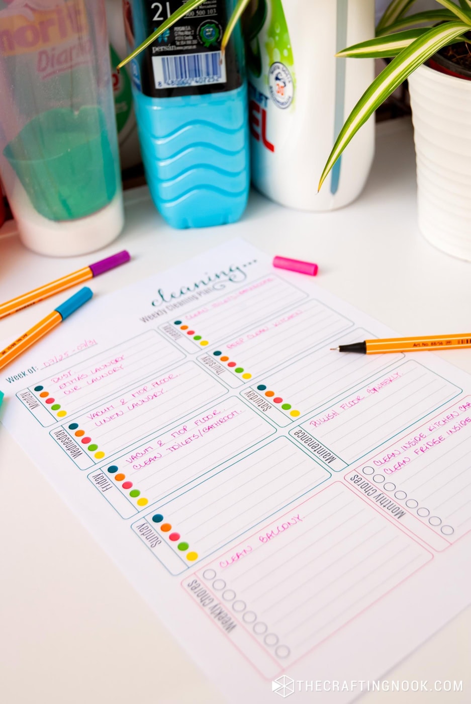 45 degree angle view of Fun Free Printable Weekly Cleaning Schedule sheet laying on top of washer machine with markers around and written tasks on it with focus point on maintenance