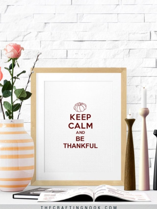 Free Keep Calm and Be Thankful Fall printable displayed in a wood frame on a decorated shelf with flowers, candles, and an open book.