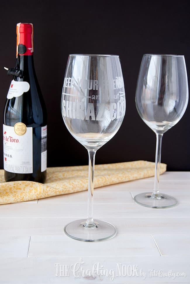 shiraz etched wine glass on table near a clean glass a wine bottle