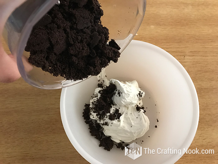 top view of crushed oreos cookies pouring over frosting inside a bowl
