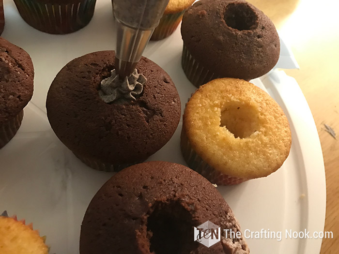 close up top view of a cupcakes being filled with frosting using a piping bag
