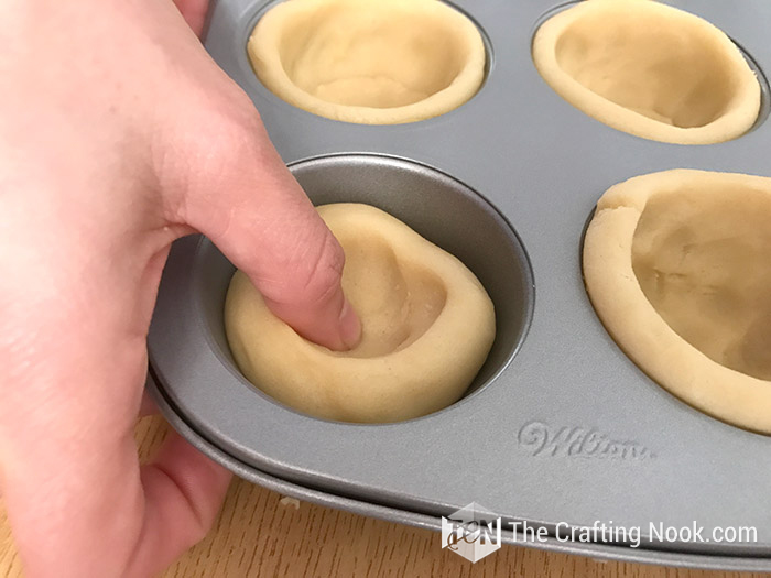 pressing the dough with the thumb towards the edges of the cupcake tray
