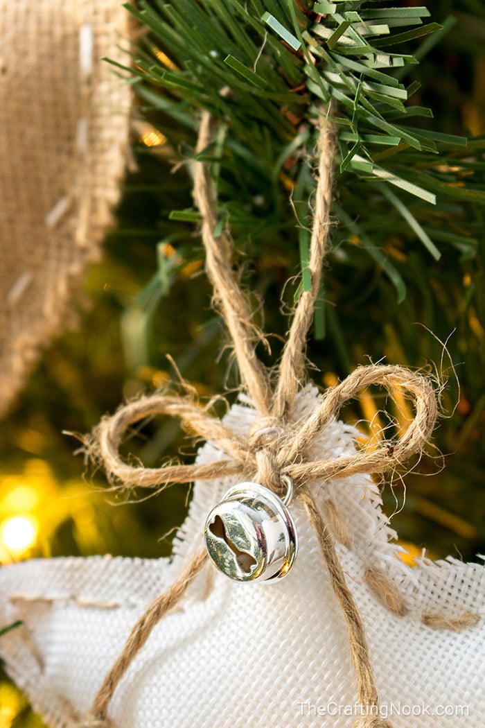 view of a cute bow made with twine and a jingle bell aganst the white burlap