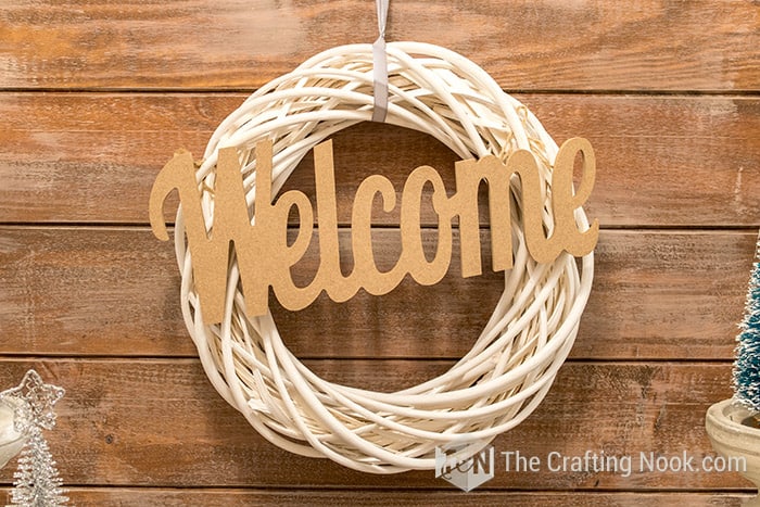 image of a wreath of rustic branches in white with the word welcome in raw wood, on a background of wooden boards
