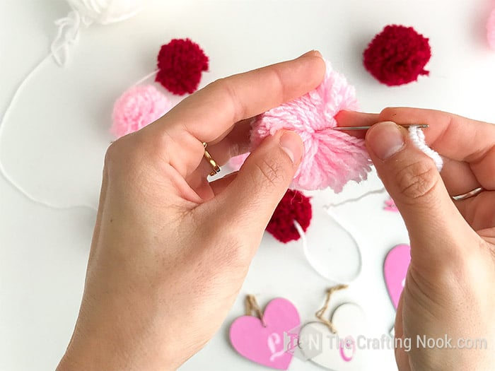 Showing exactly how to insert the needle through the center of the pom pom.