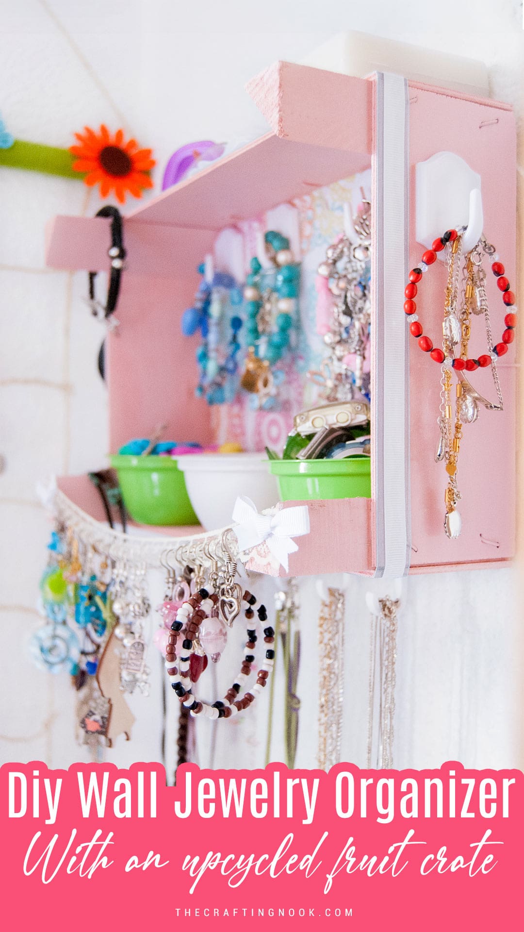 DIY Wall Jewelry Organizer With An Upcycled Fruit Cratefilled with jewelry and hanging on the wall. Pinterest image with title text overlay