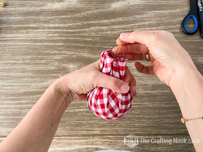 showing how to wrap the ball with the cut fabric and the gold thread to hang