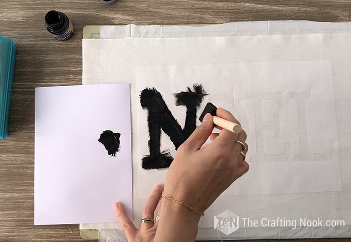 painting with black fabric paint, over the spaces of the word NOEL of the stencil on the fabric
