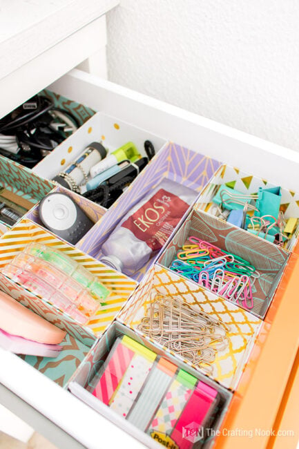 Close-up of an organized desk drawer with patterned cardstock compartments holding office supplies and small accessories.