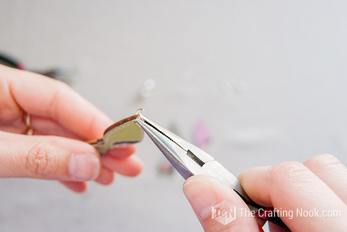 showing the pliers opening a jump ring and inserting the first wooden charm.
