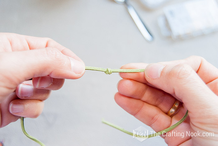 showing a knot made in the green strip of cord between the hands
