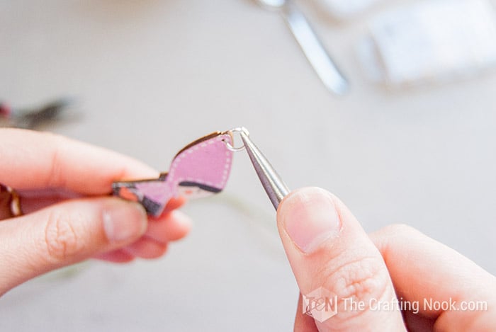 Opening a jump ring and inserting a wooden charm with the help of pliers
