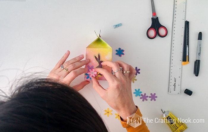 Decorating the box around the cutouts with colorful paper flowers