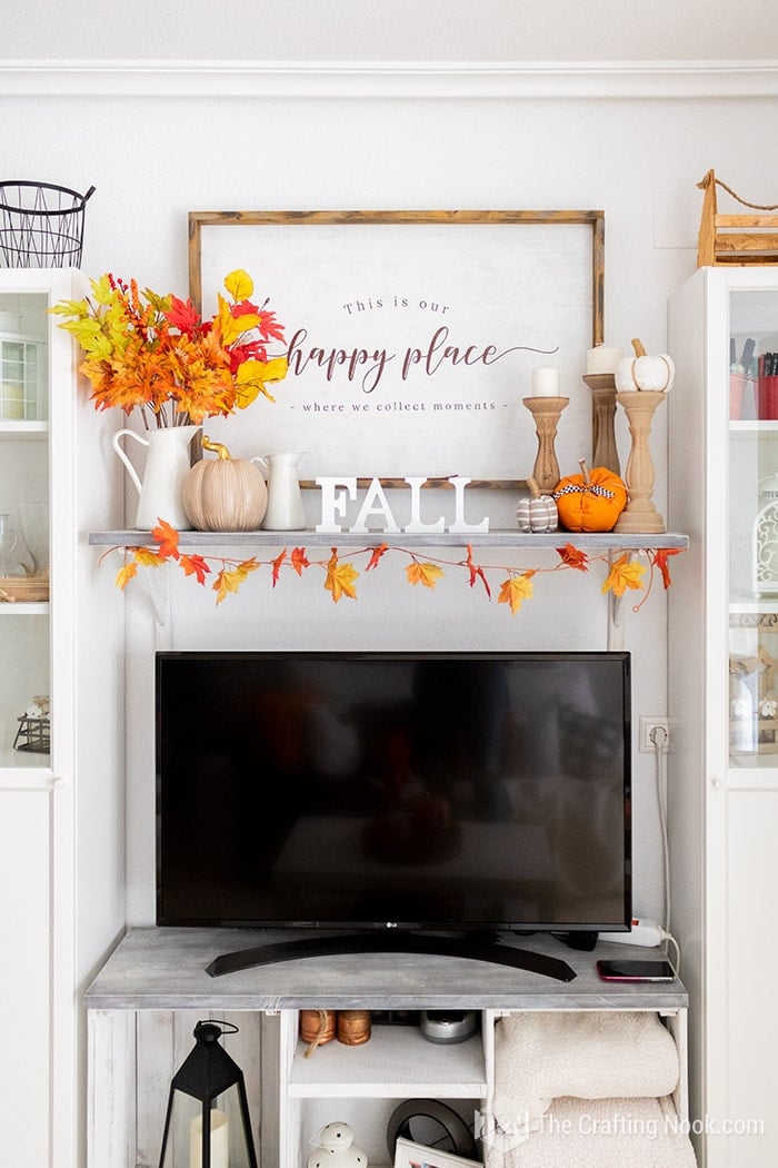 Simple mantel arrangements with stems of autumn maple leaves and pumpkins arranged around the sconce