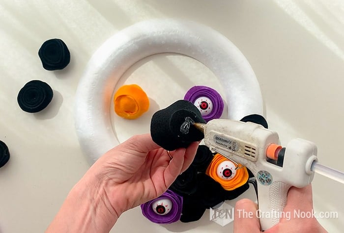 applying hot glue on the felt flowers to stick them to the wreath foam