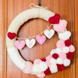 DIY Rustic Valentine Wreath with yarn, pom poms and hearts. Feature image with title text overlay