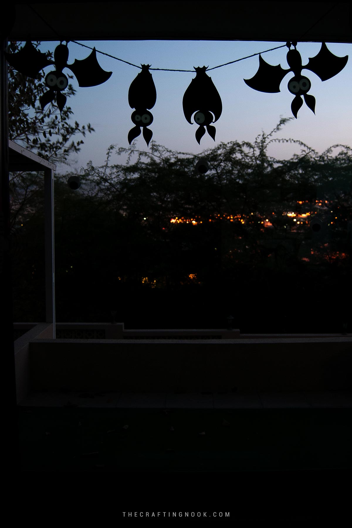 Spooky Halloween Paper Bats Garland hanging from a window at sunset Cover Image