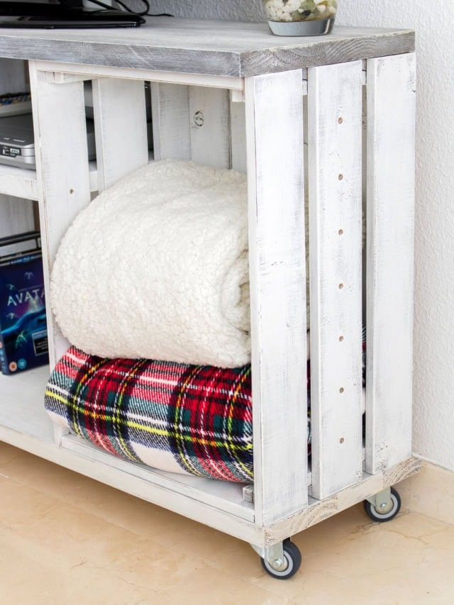 White distressed wood cart with folded blankets, DIY furniture project.