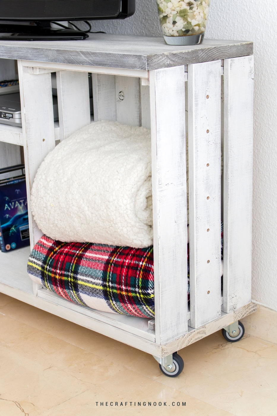 White distressed wood cart with folded blankets, DIY furniture project.