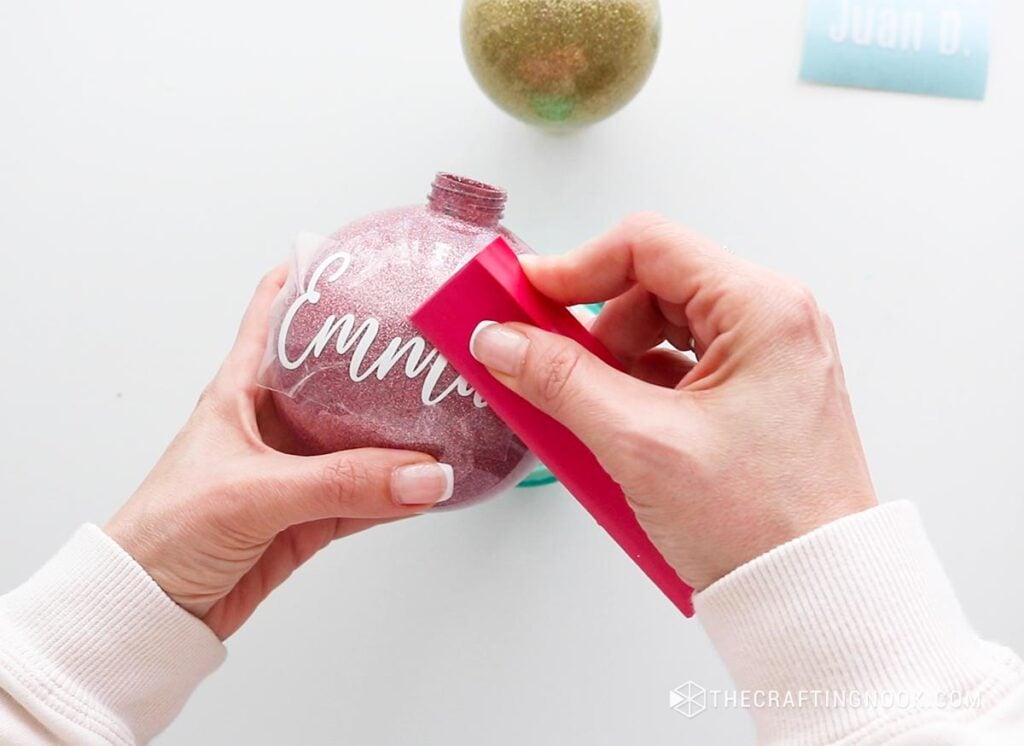 Using the scraper tool to smooth out the vinyl on the pink ornament