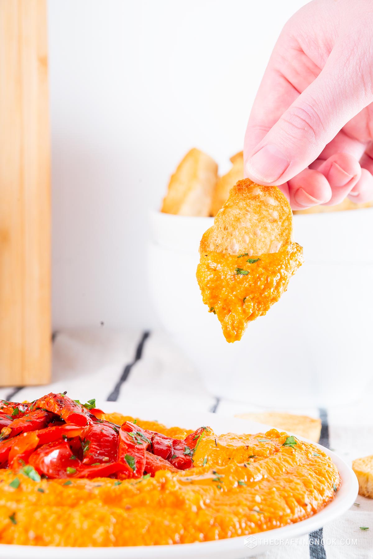 Homemade Roasted Red Pepper Hummus Recipe in a dish decorated with roasted pepper strips and me a toast dripping hummus.