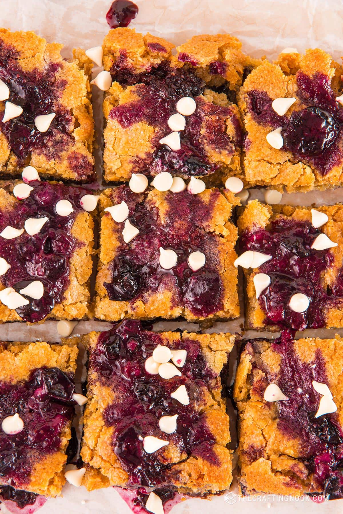 CLoseup of the White Chocolate Blueberry Blondies cut in nineths on a piece ofpartchment paper and a cutting board.