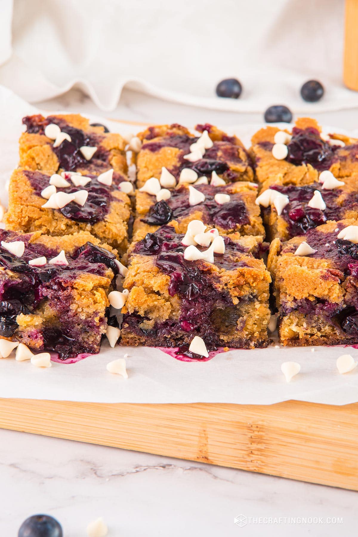 45 angle view of the White Chocolate Blueberry Blondies cut in nineths on a piece ofpartchment paper and a cutting board.