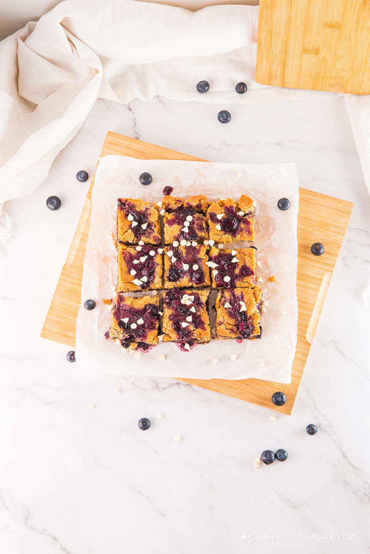 White Chocolate Blueberry Blondies cut in nineths on a piece ofpartchment paper and a cutting board.