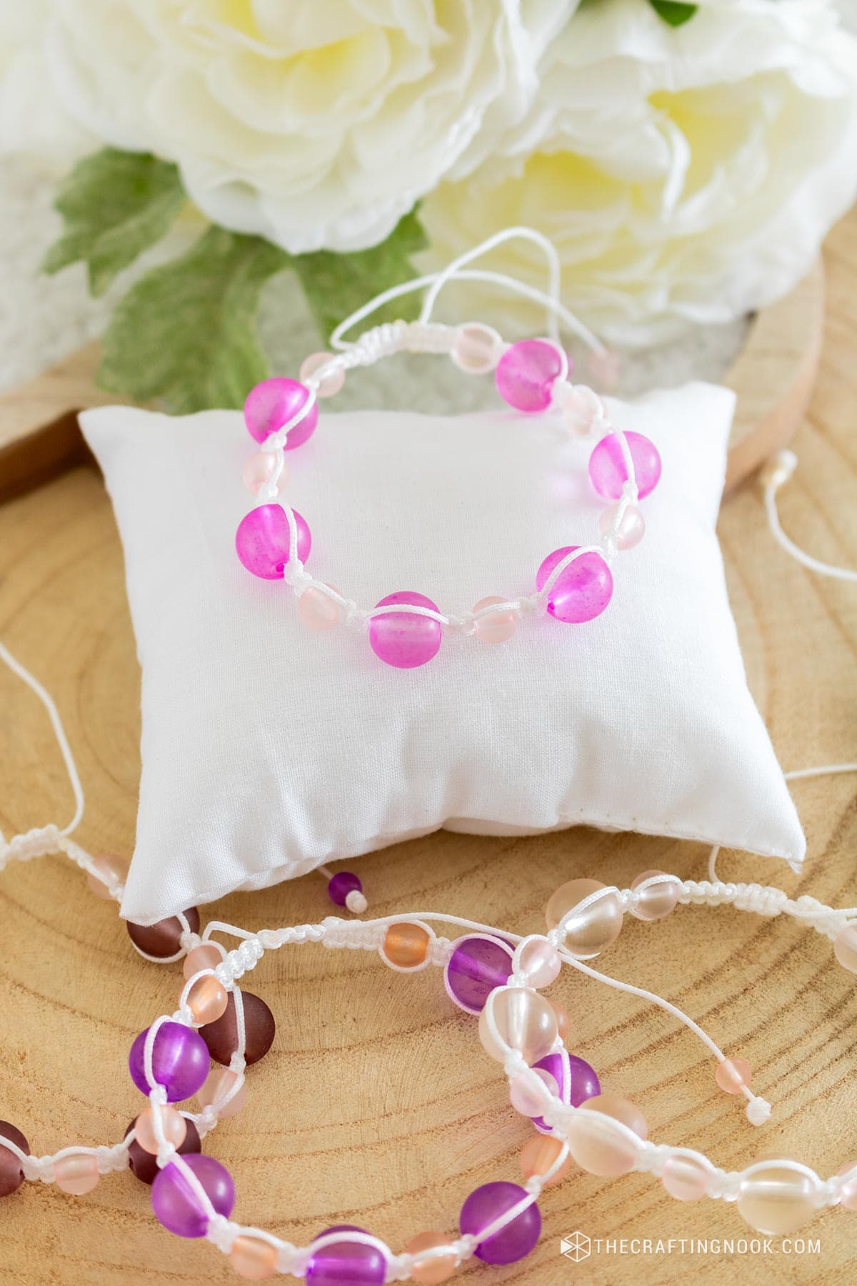 DIY macrame bracelet with beads on top of a jewelry pillow on a woodenboard with other bracelets