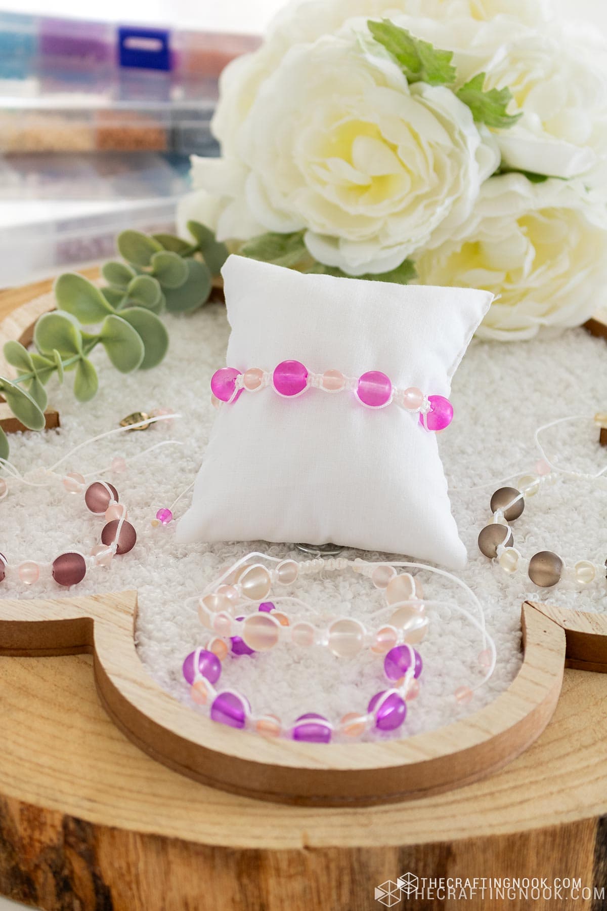 DIY macrame bracelet with beads around a jewelry pillow on a tray with other bracelets