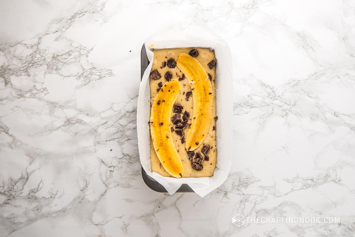 top view of whole mixture poured into baking mold with banana strips and chocolate pieces
