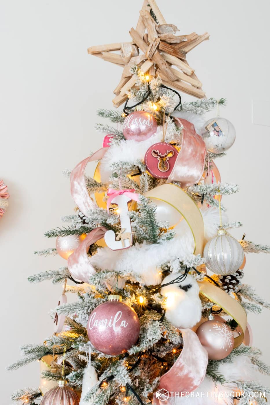 Top third of the tree with snow globe ornament, a pink glitter ornament written Blessed on it and a pink wooden, ornemante with a deer cutout, a J wooden ornament, an owl, and pink and gold ribbon