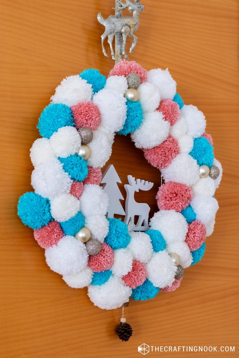 45 dregree side view of the DIY White, Pink and Blue Pompom Wreath for Christmas hanging on the door.