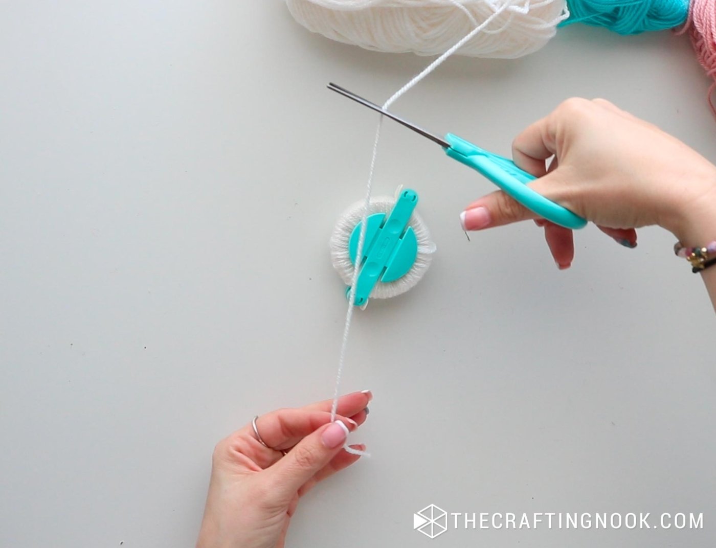 image above cutting a piece of yarn to tie the pompom in half through the pompom maker